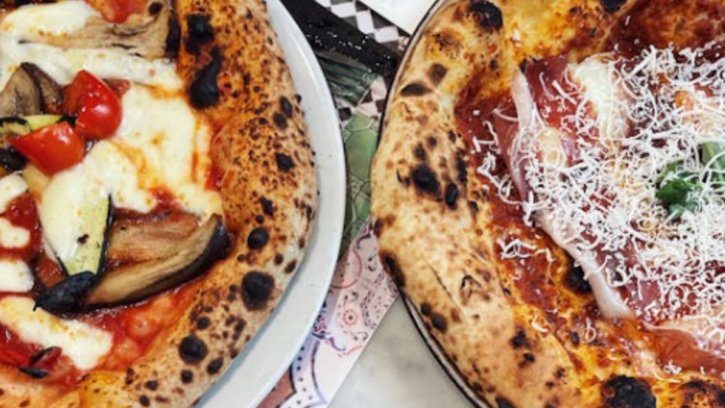 A close-up of three Neapolitan-style wood-fired pizzas.