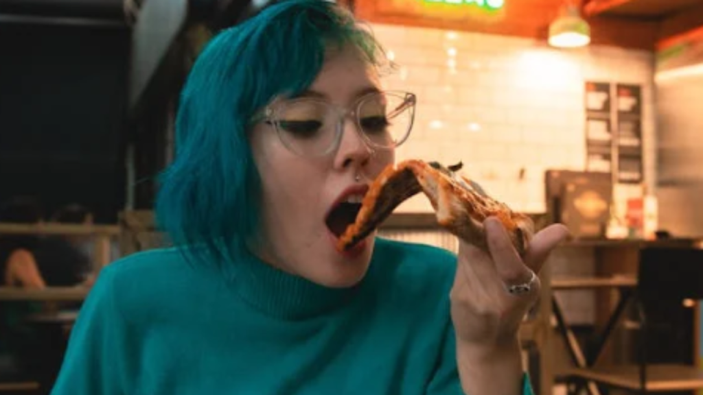 A woman takes a bite of a slice of pizza in a casual pizzeria