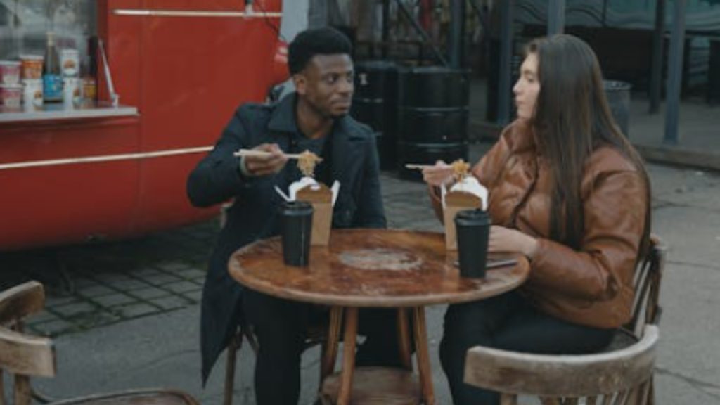 Couple eating street food at outdoor table by red food truck.