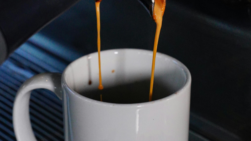 Fresh espresso pouring from a coffee machine into a white mug,