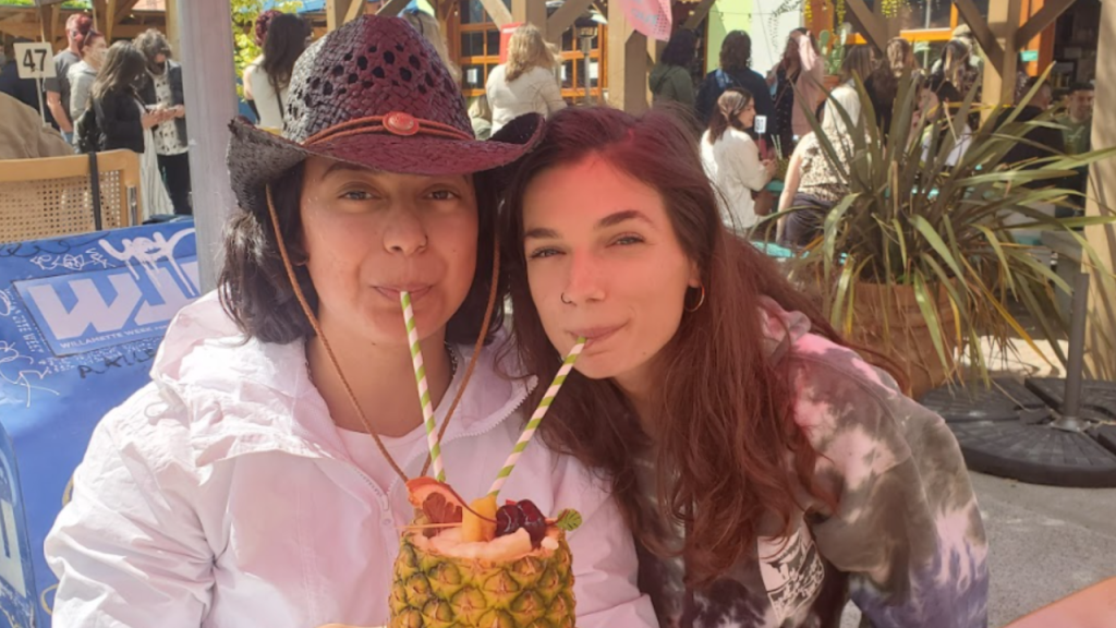 Women outdoors at a café, sharing a pineapple drink with straws during a guided food tour by Portland by Mouth.